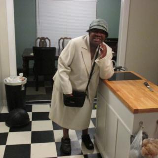 A person dressed warmly in a coat and hat standing in a kitchen.