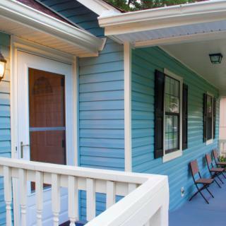 A cozy porch with blue siding, featuring a railing and two chairs.