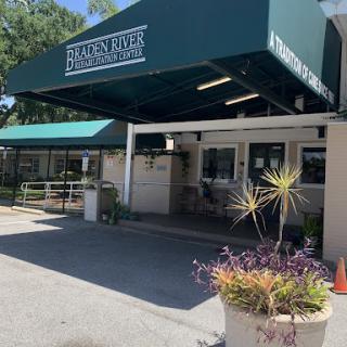 Entrance of a facility with a green canopy and decorative plants.