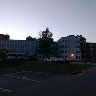 A view of a hospital building during the evening, featuring trees and a parking area.
