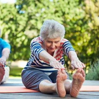 An elderly person doing a yoga stretch outdoors on a sunny day.