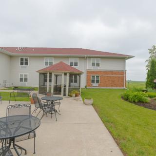 A two-story building with a patio featuring outdoor furniture, surrounded by a garden under an overcast sky.