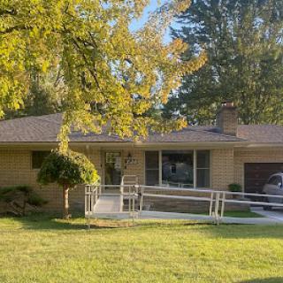 A cozy single-story house with a front ramp and lush green surroundings.