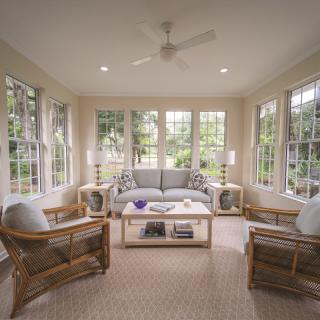 A cozy sunroom with abundant natural light, featuring comfortable seating and large windows.