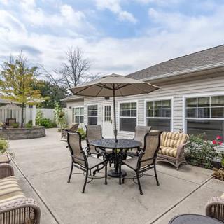 A cozy patio area with a round table, chairs, and an umbrella set against a one-story house.