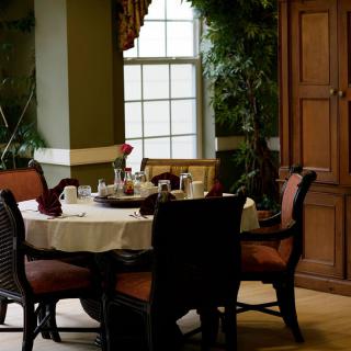 A cozy dining area with a round table set for breakfast, surrounded by upholstered chairs and illuminated by natural light from a large window.