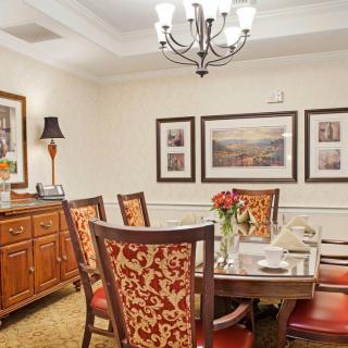 A well-appointed dining room features a large wooden table surrounded by intricately designed chairs, with elegant artwork and a chandelier enhancing the ambiance.
