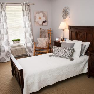 A cozy bedroom with a wooden bed, decorative pillows, and a rocking chair by the window.