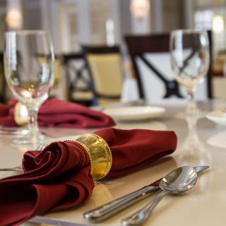 A beautifully set dining table in a restaurant with red napkins and crystal glasses.