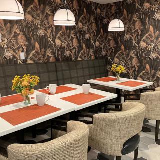 A stylish restaurant dining area featuring patterned wallpaper, cushioned seating, and neatly set tables adorned with flowers.