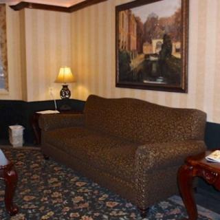 A cozy living room with a brown sofa, side tables, and a lamp, decorated with a large painting and patterned carpet.
