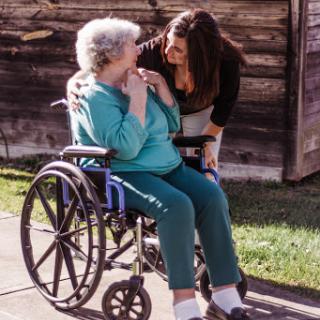 A tender moment shared between a caregiver and an elderly woman in a wheelchair.