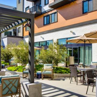A modern apartment courtyard with outdoor seating and a pergola under sunny skies.