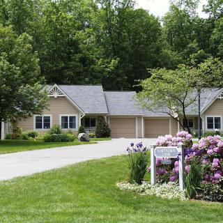 A single-story house with a well-maintained front yard, featuring flowers and a tree-lined driveway.