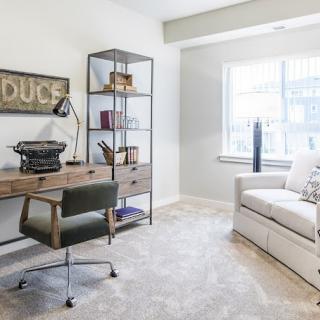 A bright and cozy home office with a desk, typewriter, shelves, and a comfortable seating area.