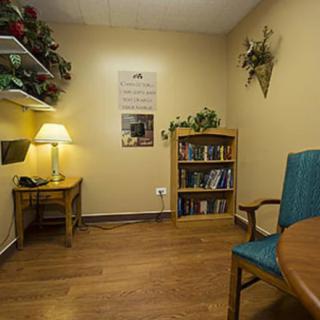 A cozy office space with a lamp, bookshelf, and seating.