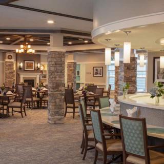 A spacious and elegantly designed dining area with multiple tables and chairs, featuring modern lighting and stone columns.