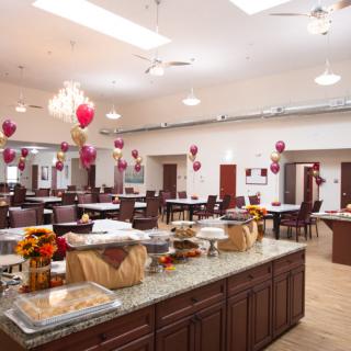A spacious dining hall decorated with balloons and set up for an event, featuring neatly arranged tables and a central counter.