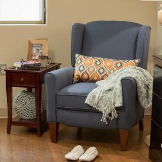 A cozy living room corner with a blue armchair and a decorative pillow, complemented by a side table and slippers on the floor.