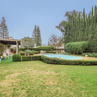 A spacious backyard featuring a swimming pool surrounded by lush greenery and well-maintained hedges.