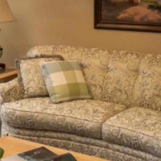 A cozy living room with a patterned sofa, adorned with a plaid cushion, next to a lamp and artwork.