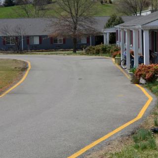 A suburban road with yellow lines, flanked by houses and trees.