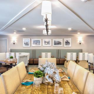A modern dining room with a long table, upholstered chairs, and elegant lighting, showcasing framed art on the walls.