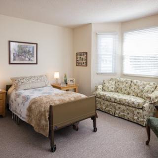 A cozy and well-furnished bedroom featuring a single bed, a floral sofa, and natural light streaming through the windows.