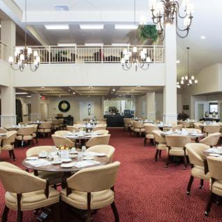 A spacious and elegantly designed dining room featuring round tables and comfortable chairs, adorned with chandeliers.