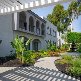A beautiful courtyard with lush greenery and a shaded walkway in front of a two-story building.