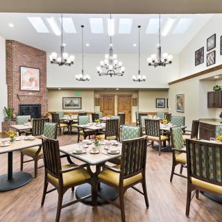 A well-lit dining room with elegant chandeliers, neatly arranged tables and chairs, and stylish decor.