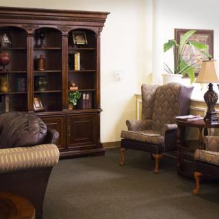 A cozy living room features a large wooden bookshelf, two upholstered armchairs, and a lamp.
