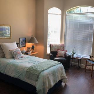 A cozy bedroom with a single bed, large windows, and warm decor.