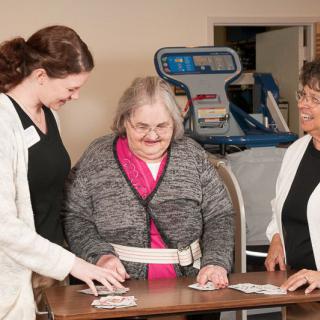 An elderly woman is engaged in a rehabilitation activity with the assistance of two healthcare workers.