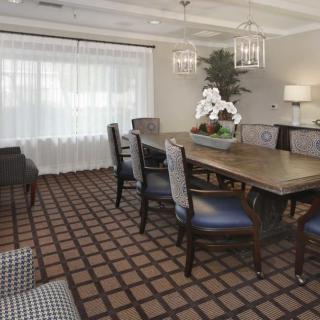 A well-furnished dining or meeting room featuring a large wooden table, upholstered chairs, a patterned carpet, and elegant chandeliers.