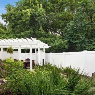 A serene garden with a white pergola and fence, surrounded by lush greenery.