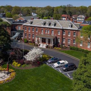 An aerial view of a large brick building surrounded by greenery and parked cars.