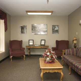 A cozy waiting room with chairs and a sofa around a coffee table, decorated with flowers and artwork on the walls.