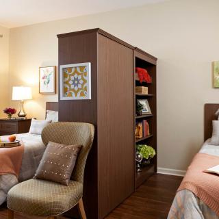 A shared bedroom featuring two beds separated by a central bookshelf, with cozy decor and warm lighting.