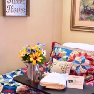 A cozy bedroom setup featuring a colorful quilt, fresh flowers in a vase, and warm home decor accents.