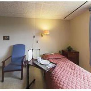 A simple hospital room with a bed, chair, and bedside table.