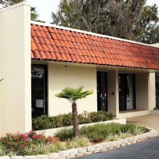 A small building with a red-tiled roof and surrounding landscaping, including a palm tree.