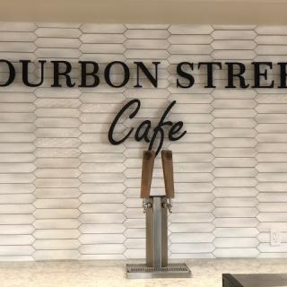 Sign for Bourbon Street Cafe with modern white brick wall background.