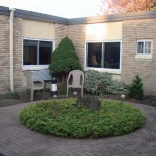 A small courtyard with a circular garden, surrounded by a brick building and featuring chairs and a table.