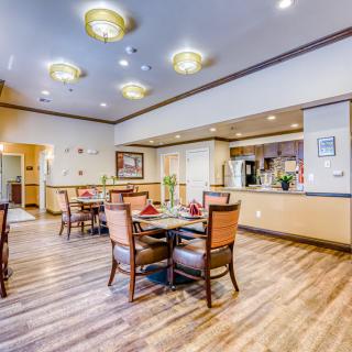 A well-lit dining room with wooden flooring, featuring tables and chairs arranged neatly.