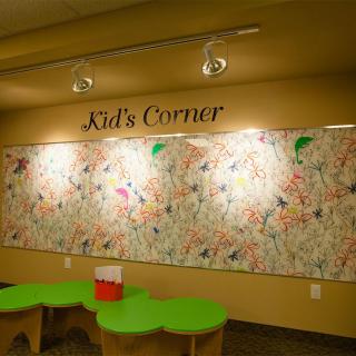 A children's play space called 'Kid's Corner' featuring a colorful and artistic wall, accompanied by green tables.
