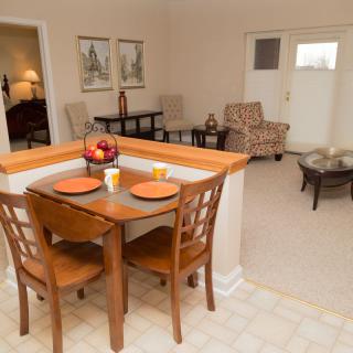 A cozy apartment interior featuring a small dining area with a wooden table and chairs, leading into a living room with comfortable seating.