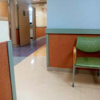 A quiet waiting area in a hospital, featuring a single green chair and a glimpse of the corridor.