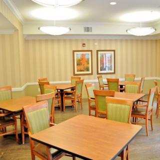 An empty dining room with wooden tables and chairs, softly lit from above.