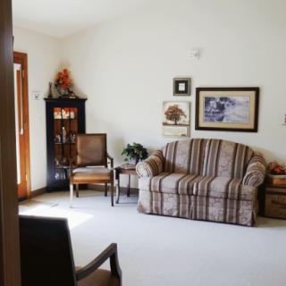 A cozy living room with a striped sofa, wooden chair, and wall decorations.